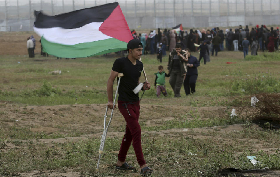 A wounded protesters waves his national flag as others gather near the fence of Gaza Strip border with Israel, marking first anniversary of Gaza border protests east of Gaza City, Saturday, March 30, 2019. Tens of thousands of Palestinians on Saturday gathered at rallying points near the Israeli border to mark the first anniversary of weekly protests in the Gaza Strip, as Israeli troops fired tear gas and opened fire at small crowds of activists who approached the border fence. (AP Photo/Adel Hana)