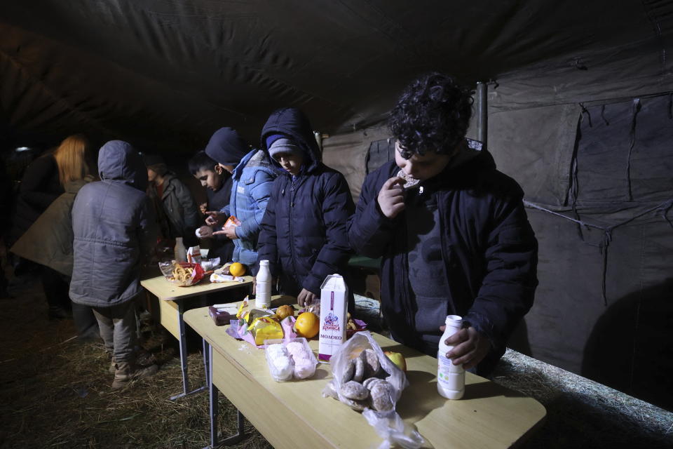 Migrants eat food delivering by Belarusian volunteers as they gather at the Belarus-Poland border near Grodno, Belarus, Saturday, Nov. 13, 2021. A large number of migrants are in a makeshift camp on the Belarusian side of the border in frigid conditions. Belarusian state news agency Belta reported that Lukashenko on Saturday ordered the military to set up tents at the border where food and other humanitarian aid can be gathered and distributed to the migrants. (Leonid Shcheglov/BelTA pool photo via AP)