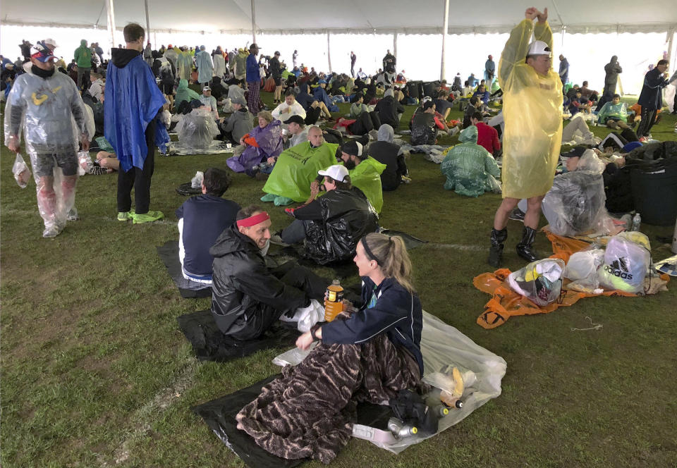 FILE - In this April 15, 2019, file photo, runners wait under a tent while it rains before the start of the 123rd Boston Marathon in Hopkinton, Mass. Organizers of the marathon, postponed indefinitely because of the coronavirus pandemic, have launched a virtual Athletes' Village in 2020 to reproduce at least some of the camaraderie of the real thing. (AP Photo/Jennifer McDermott, File)