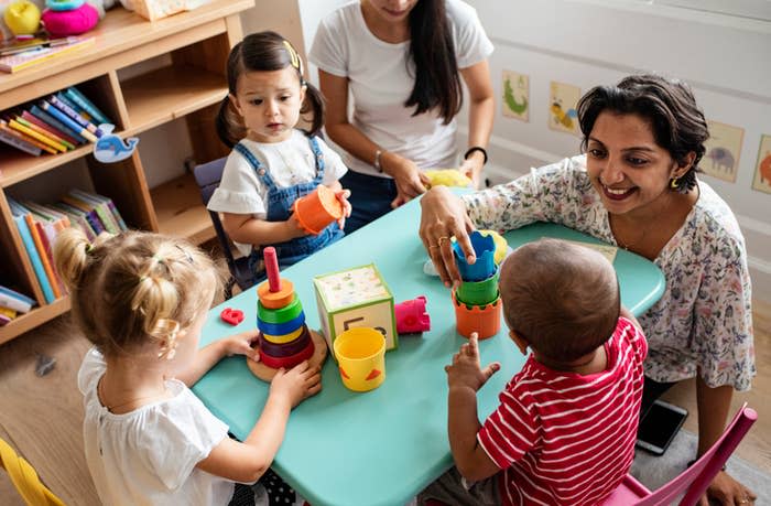 Adult supervising three young children playing with educational toys at a table