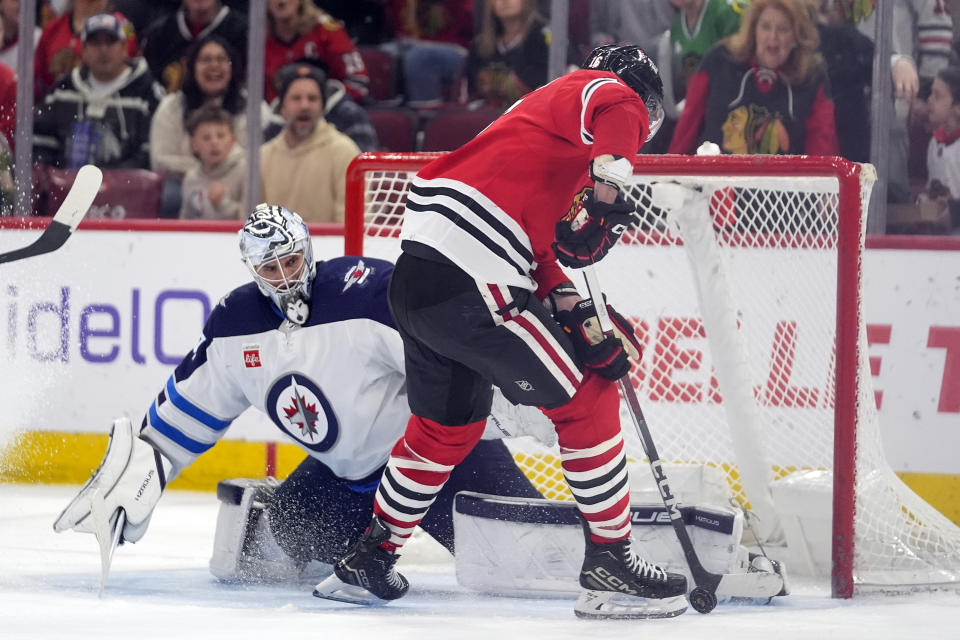 Winnipeg Jets goaltender Connor Hellebuyck, left, makes a save against Chicago Blackhawks center Jason Dickinson, right, during the second period of an NHL hockey game Friday, Feb. 23, 2024, in Chicago. (AP Photo/Erin Hooley)