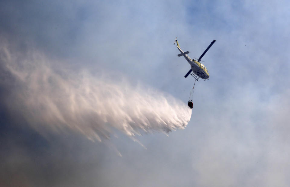 A helicopter drops water over a fire at Rhodes Memorial on Table Mountain, Cape Town, South Africa, Sunday, April 18, 2021. A wildfire raging on the slopes of the mountain forced the evacuation of students from the University of Cape Town. (AP Photo/Nardus Engelbrecht)