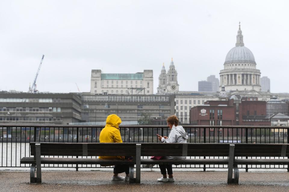People sit on a bench on Southbank in London, as many parts of the UK experience wet weather ahead of the arrival of Storm Ellen (PA)