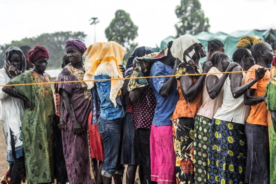 A group of women stand in the rain waiting to be registered and to receive their refugee status at Kuluba Collection Point.<br /><i>Location: Kuluba Collection Point, Nov. 1, 2016.</i>