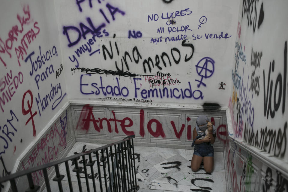 Una niña de 10 años víctima de abusos sexuales, que se cubre la cara para ocultar su identidad, juega con su chihuahua Miel en una escalera cubierta con pintadas contra la violencia sexual en la sede de la Comisión Nacional de los Derechos Humanos, ocupada desde hace casi tres meses por activistas feministas y convertida en un refugio para víctimas de violencia de género, en la Ciudad de México, el 17 de noviembre de 2020. La pequeña vive en el inmueble con su madre, Erika Martínez, quien también sufrió abusos sexuales. Martinez dijo que hace tres años denunció ante la fiscalía para delitos sexuales que su hija, que entonces tenía 7, fue abusada por su cuñado, pero el hombre sigue libre. (AP Foto/Ginnette Riquelme)