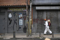 A city worker sprays disinfectant on shuttered storefronts in the Catia neighborhood of Caracas, Venezuela, Saturday, Aug. 8, 2020, amid the new coronavirus pandemic. (AP Photo/Matias Delacroix)