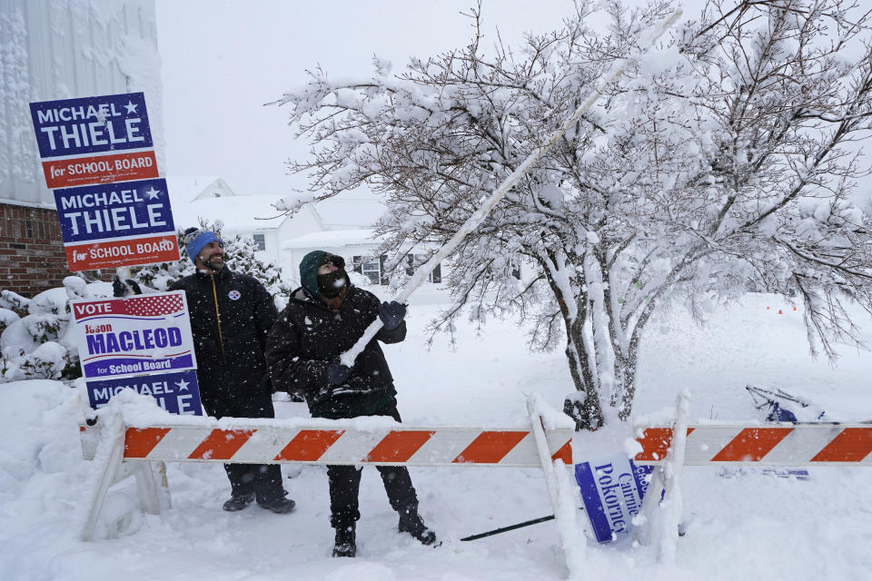 Cairnie Pokorney, right, a school board candidate, clears snow from a tree that was dropping on his head, while campaigning on Election Day, Tuesday, March 14, 2023, in Derry, N.H. By the time the winter storm wraps up Wednesday, snow totals in New England are expected to reach a couple of feet of snow in higher elevations to several inches along the coast. At left is Michael Thiele, also a school board candidate. (AP Photo/Charles Krupa)