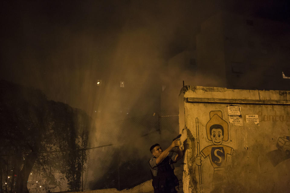 A Police officer of the Pacifying Police Unit, patrols among the smoke from burning barricades during clashes at the Pavao Pavaozinho slum in Rio de Janeiro, Brazil, Tuesday, April 22, 2014. Intense exchanges of gunfire, numerous blazes set alit and a shower of homemade explosives and glass bottles onto a busy avenue in Rio de Janeiro’s main tourist zone erupted Tuesday night after the death of a popular young shantytown resident. (AP Photo/Felipe Dana)