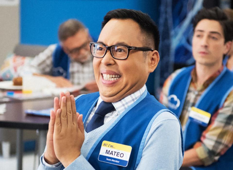 Mateo from "Superstore" smiling and clapping, seated in the breakroom with co-workers behind him