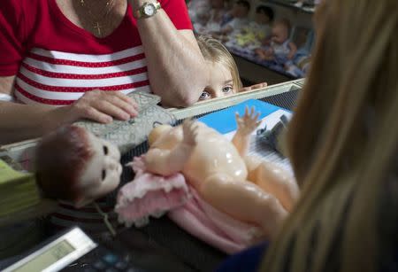 A young customer looks over the counter as a family member brings in a doll for repair at Sydney's Doll Hospital May 20, 2014. REUTERS/Jason Reed