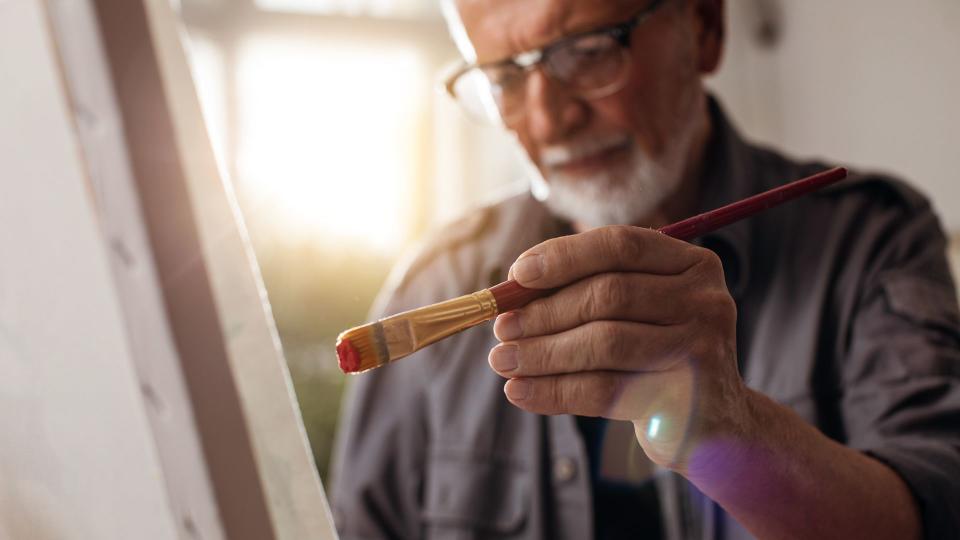 Close up shot of an older man painting on canvas.