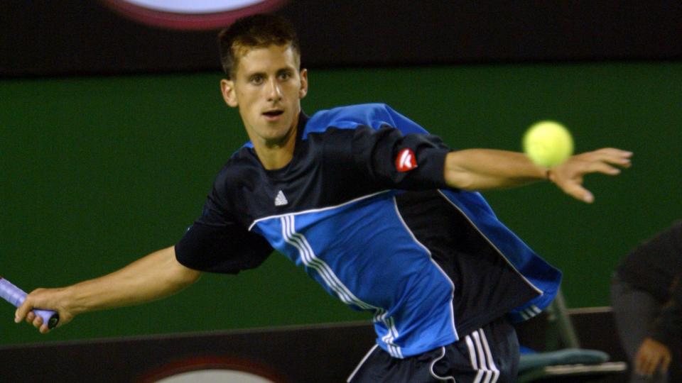 novak djokovic watches a tennis ball as he prepares to hit it on the run, he wears a black and blue adidas jersey and shorts