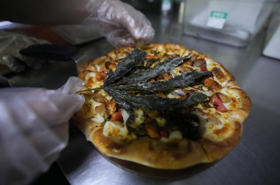 A staff member decorates a pizza with a deep fried cannabis leaf at a restaurant in Bangkok, Thailand on Nov. 24, 2021. The Pizza Company, a Thai major fast food chain, has been promoting its "Crazy Happy Pizza" this month, an under-the-radar product topped with a cannabis leaf. It’s legal but won’t get you high. (AP Photo/Sakchai Lalit)