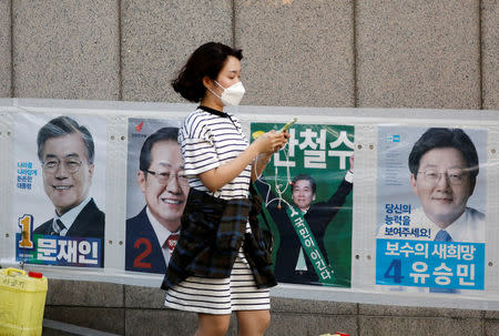 A woman holding her mobile phone walks past posters of candidates for the upcoming May 9 presidential election in Seoul, South Korea, May 7, 2017. REUTERS/Kim Hong-Ji