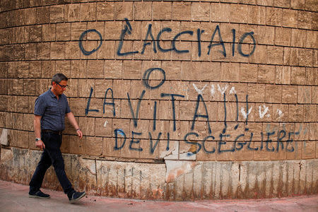 A man walks past a graffiti reading "Steel or life, you have to choose" in the Tamburi district, in Taranto, southern Italy April 27, 2018. Picture taken April 27, 2018. REUTERS/Tony Gentile