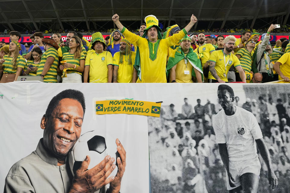 Aficionados de Brasil alientan a la selección detrás de un cartel con imágenes de Pelé, el lunes 5 de diciembre de 2022, antes de un partido del Mundial ante Corea del Sur en Al Rayán, Qatar (AP Foto/Martin Meissner)