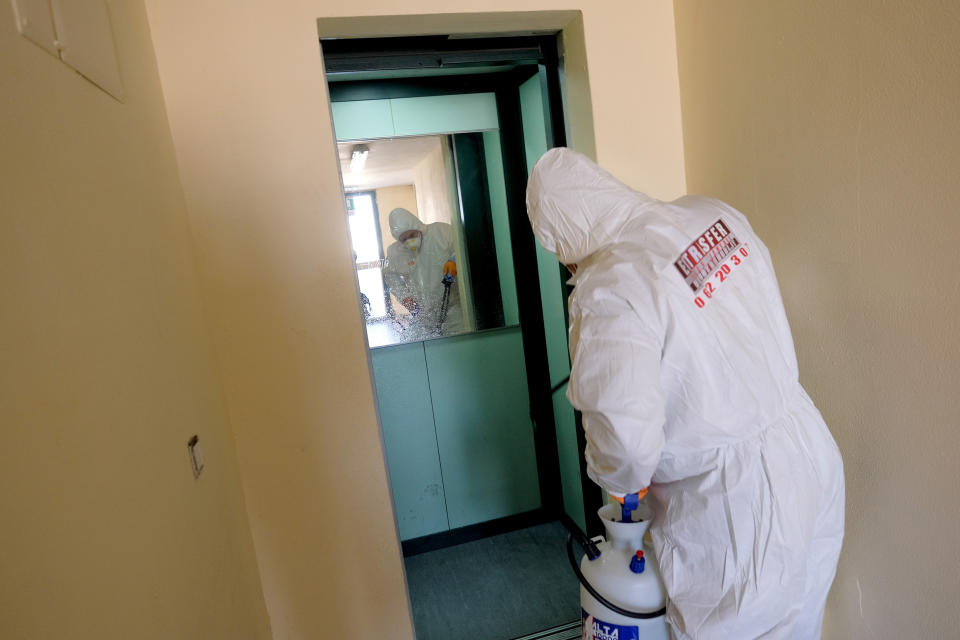 A man wearing a protective suit sanitizes the elevator of a public housing building to prevent the spreading of the coronavirus, in the neighborhood of Spinaceto, on the outskirts of Rome, Monday, March 30, 2020. The new coronavirus causes mild or moderate symptoms for most people, but for some, especially older adults and people with existing health problems, it can cause more severe illness or death. (Mauro Scrobogna/LaPresse via AP)