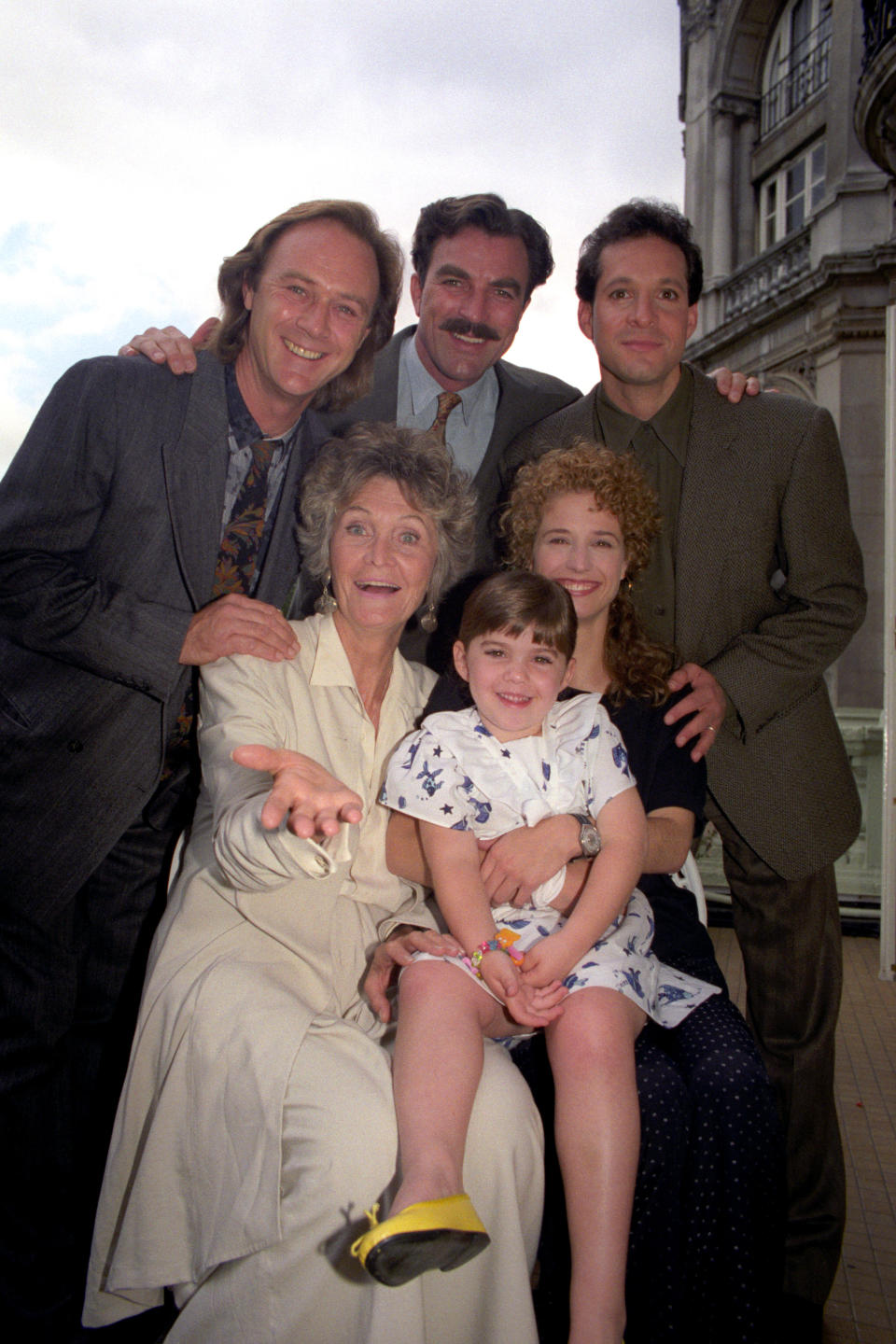 The cast of the film "Three Men and a Little Lady" in London before shooting for three weeks on location in Stratford-upon-Avon. From left (back row) Christopher Cazenove, Tom Selleck and Steve Guttenberg. Front Row: Sheila Hancock, Robin Wiseman (child) and Nancy Travis (right).   (Photo by Sean Dempsey/PA Images via Getty Images)