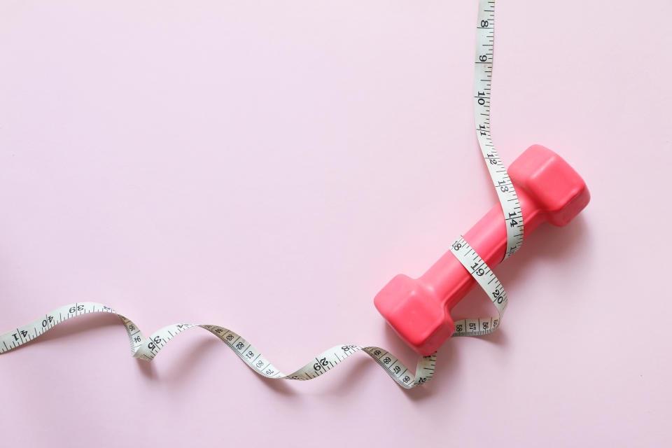 Hormones are important in regulating our appetite and energy balance. (Getty) Directly above shot of small Pink Dumbbell wrapped with measure tape on pink background. Copy space