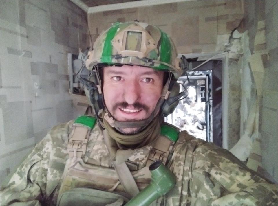 Bohdan Yatsun smiling, in uniform, in the damaged hallway of a building.