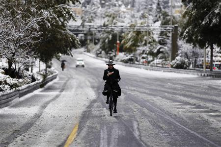 An ultra-Orthodox Jewish man rides his bicycle on a snow-covered road in winter in Jerusalem December 12, 2013. REUTERS/Amir Cohen