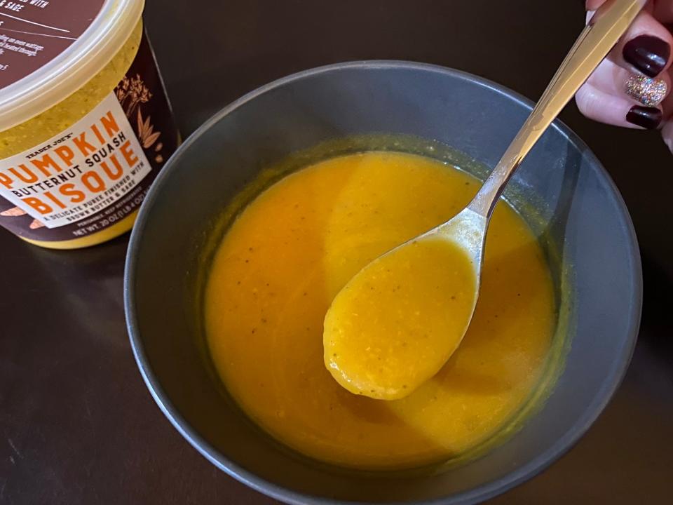 Creamy orange-y yellow soup in spoon above a bowl of soup