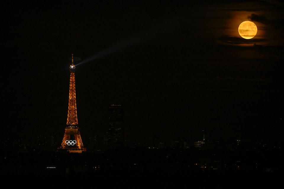 This photograph shows the Olympic rings displayed on the Eiffel Tower at night, with the full moon appearing, ahead of the Paris 2024 Olympic and Paralympic games, in Paris on July 21, 2024.