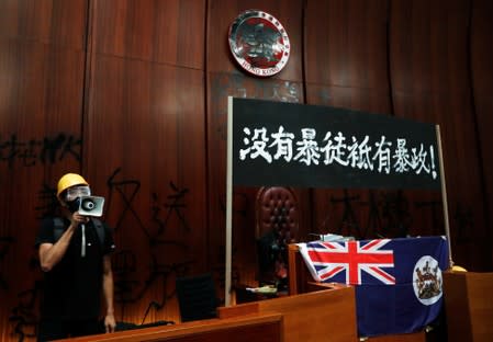 A man uses a loudspeaker as he stands next to a colonial flag of Hong Kong and a banner displayed inside a chamber, after protesters broke into the Legislative Council building during the anniversary of Hong Kong's handover to China in Hong Kong