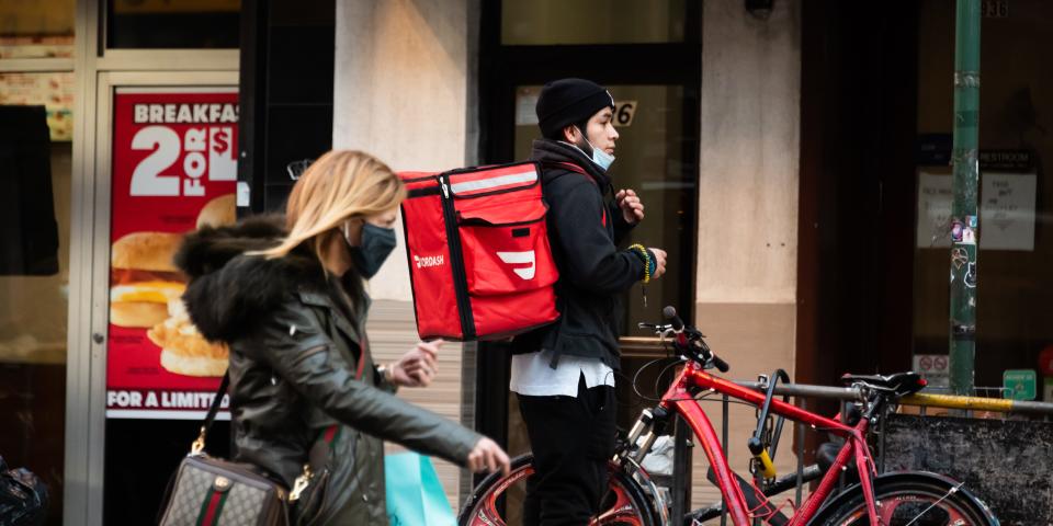 A DoorDash rider with his bike and delivery pack on his back exiting a NYC restaurant in winter.