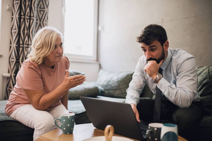 A woman and man sit together looking at a laptop; the man appears concerned or puzzled