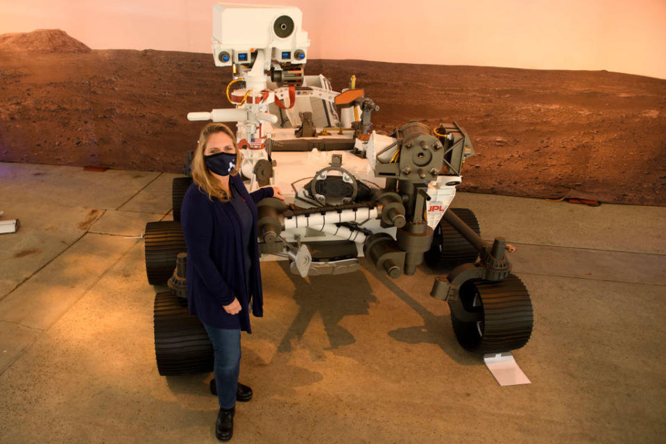 A woman standing next to a Mars rover, which is higher than she is