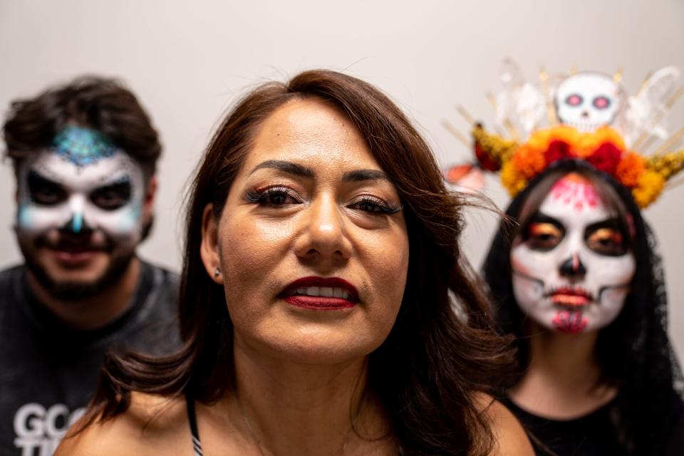 Noemi Ayala-Antonsen (center), owner of A Sweet Party, poses for a portrait after painting the faces of Raphael Romero Ruiz (left), an engagement reporter at The Arizona Republic, and her daughter, Alexa Antonsen (right), 18, during a Dia de Los Muertos face-painting demonstration at The Arizona Republic office in Phoenix on Oct. 12, 2023.
