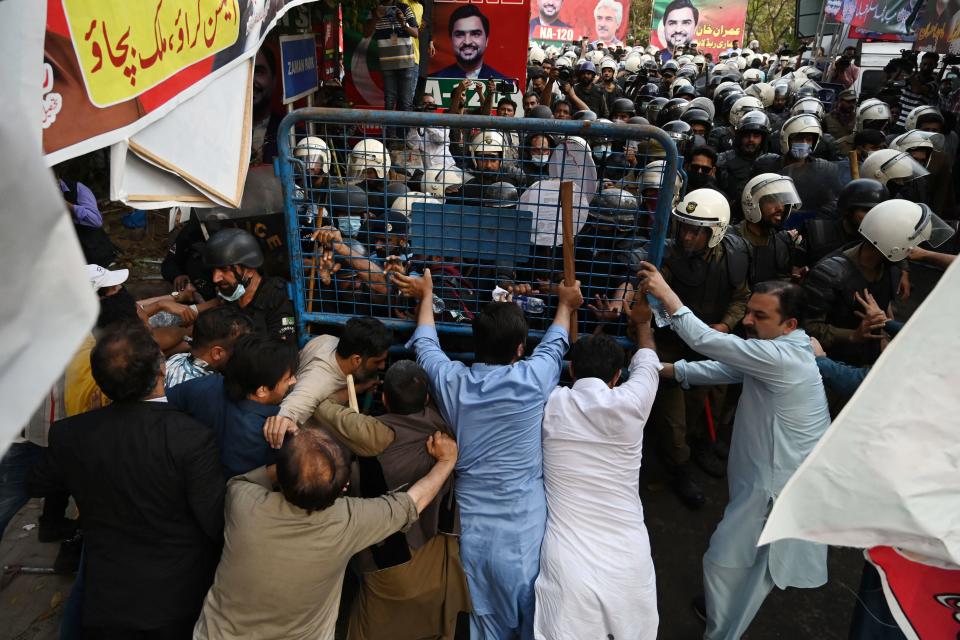 Khan supporters use what looks like a barricade to hold back a sea of helmeted troops.