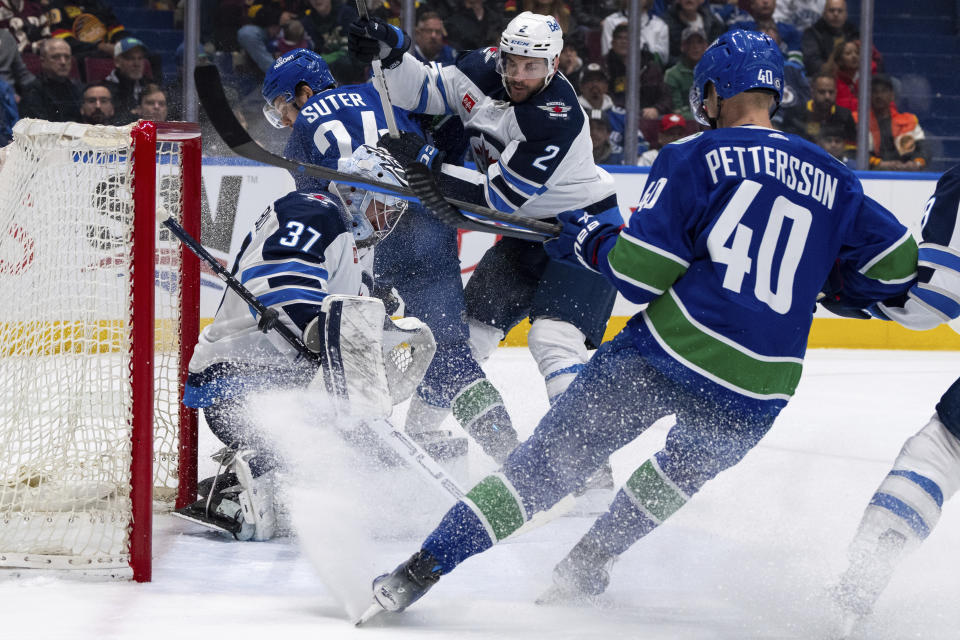 Vancouver Canucks' Nils Hoglander, not seen, scores on Winnipeg Jets goaltender Connor Hellebuyck (37) as Vancouver's Pius Suter (24) and Elias Pettersson (40) and Winnipeg's Dylan DeMelo (2) watch during the first period of an NHL hockey game Saturday, March 9, 2024, in Vancouver, British Columbia. (Ethan Cairns/The Canadian Press via AP)