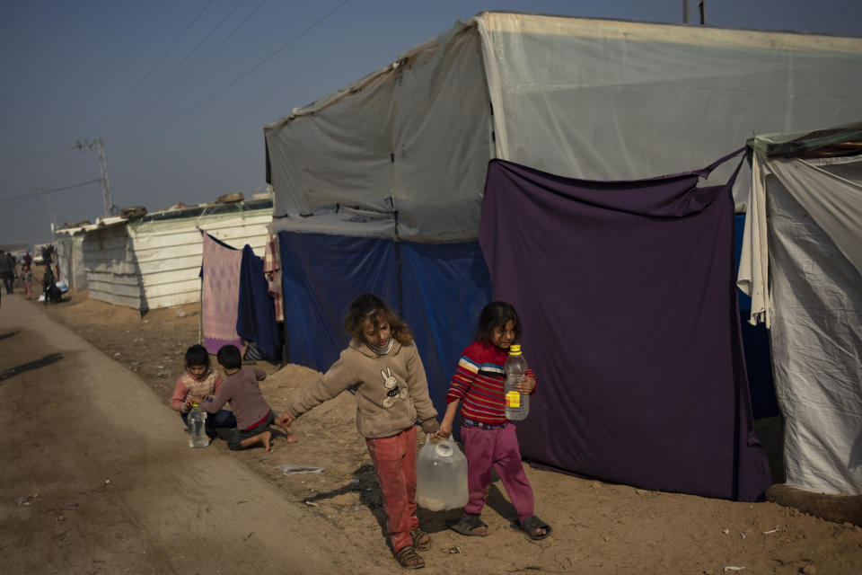 Palestinian children displaced by the Israeli bombardment of the Gaza Strip carry water in the makeshift tent camp in the Muwasi area on Monday, Dec. 18, 2023. (AP Photo/Fatima Shbair)