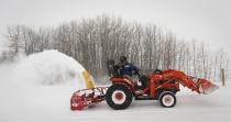 David Reid uses a snow blower mounted on a tractor to clear his driveway during a blizzard near Cremona, Alta., Monday, Dec. 2, 2013. Southern Alberta is under a winter storm warning with temperatures dipping down to -20C with high winds and heavy snowfall. THE CANADIAN PRESS/Jeff McIntosh