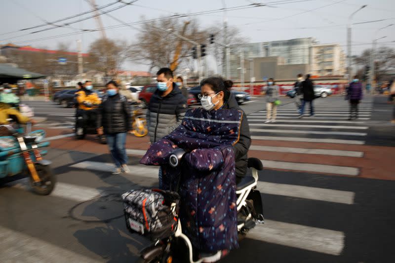 People wearing face masks ride scooters and walk on a street following an outbreak of the coronavirus disease (COVID-19), in Beijing, China