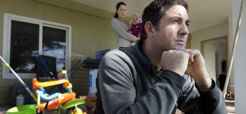 Man sits in thought while wife holds small child behind him.