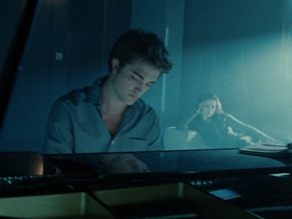 Edward playing at the piano with bella sitting and watching in the background in twilight