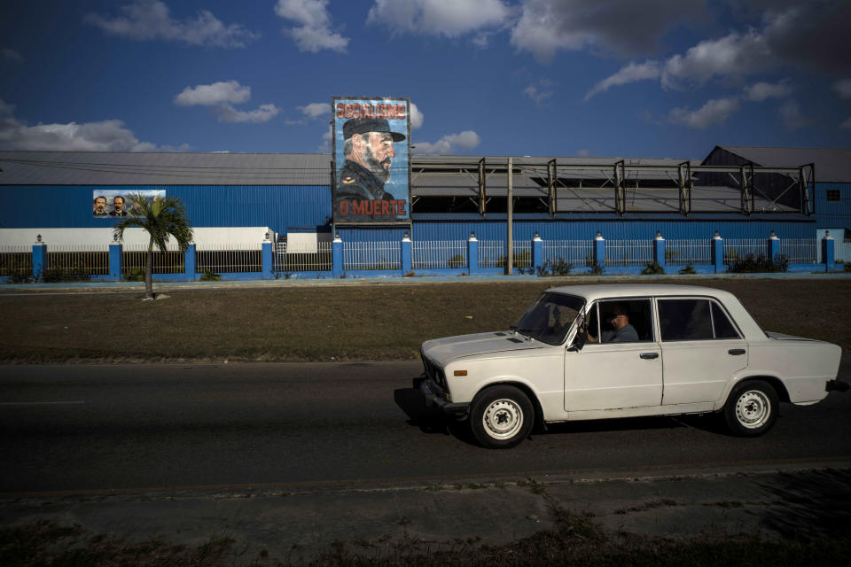 A commuter drives a Soviet-era Lada car past a billboard of the late Fidel Castro with the words "Socialism or Death" written on it in Havana, Cuba, Monday, March 22, 2021. When the Ladas arrived in Cuba they were turned into taxis by the thousands and some went to government offices, the leaders of the Communist Party, and prominent workers. (AP Photo/Ramon Espinosa)