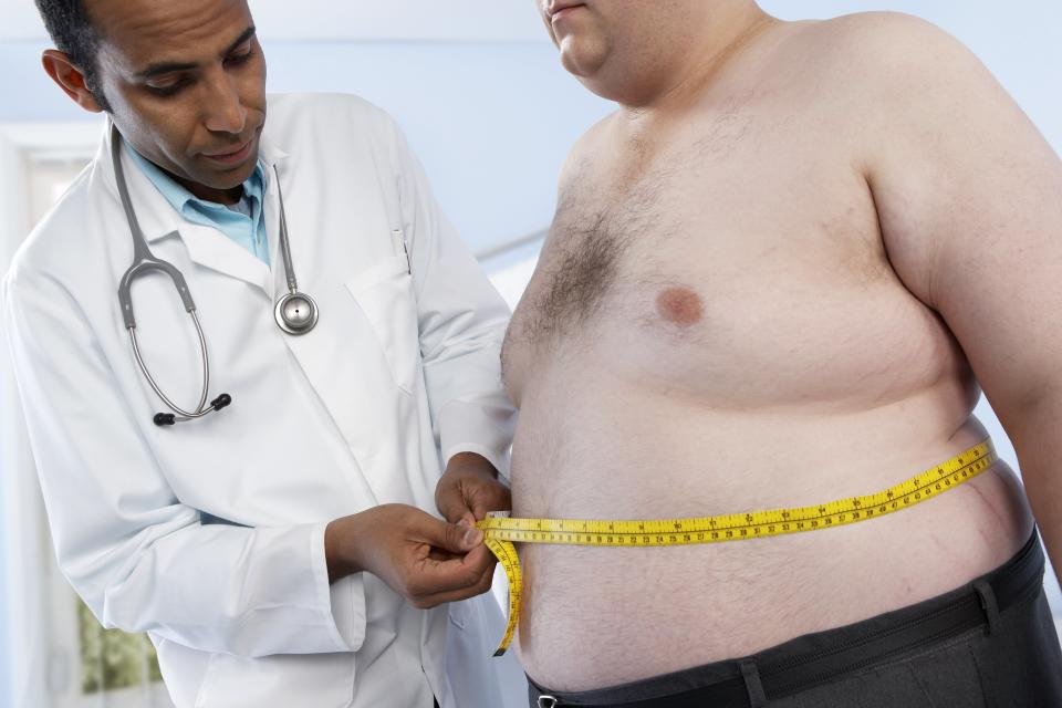 A doctor measures the waist of an obese patient