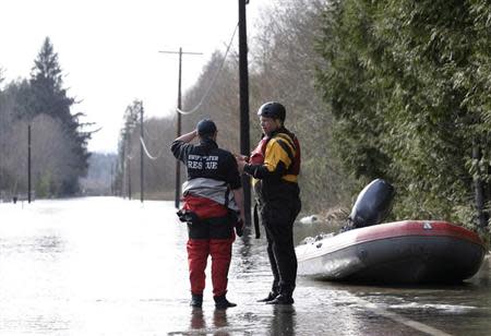 Search and rescue workers stand along a flooded portion of Highway 530 down the road from a massive landslide outside Darrington, Washington March 24, 2014. REUTERS/Jason Redmond