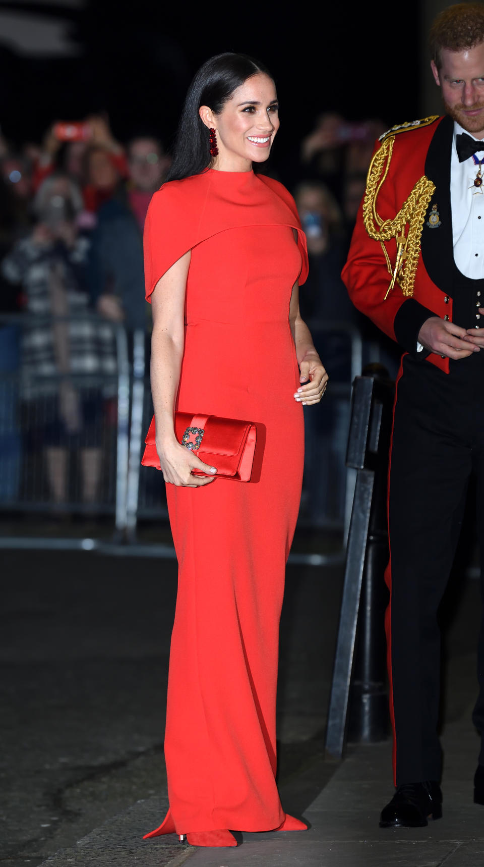 <p> In an all-red look (and matching with Prince Harry's Royal Marines officer's mess jacket, which I love), Meghan took the traditional royal tonal dressing to new chicness to one of the couple's last official events as senior royals. The red cape Safiyaa gown (you can't see it in that photo, but a piece of fabric trails down the back to the floor) is, as with the best of her looks, simple but regal at the same time. The clutch is Manolo Blahnik and the shoes Aquazurra. </p>