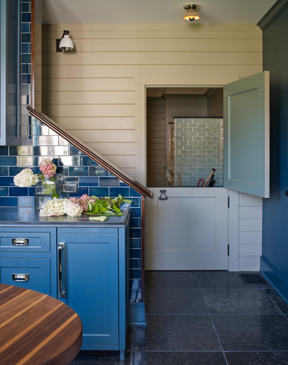 This photo captures one of the home’s in-between spaces. The front section is a butler’s pantry with a blue-tiled staircase that leads to a bunk room above the garage, the rear of an enormous mudroom divided by a Dutch door. “Janice and Lee wanted a Dutch door because they have a large family of dogs. The dogs hang out in the mudroom,” says Lippmann. “They have little cubbies. That silvery green tile you see—it’s actually a dog wash.” (The family uses the space too. “Every[one] has their own cubby with hooks for their jackets and places for their boots.”) The green tile in the mudroom is by Pratt & Larson. Both sets of tile were installed by Old Port Specialty Tile. Farrow & Ball paints Green Smoke and London Stone were used for the upper half of the Dutch door and for the wall of the pantry respectively. Lighting is by Urban Electric; hardware is by Hamilton Sinkler and Horton Brasses.