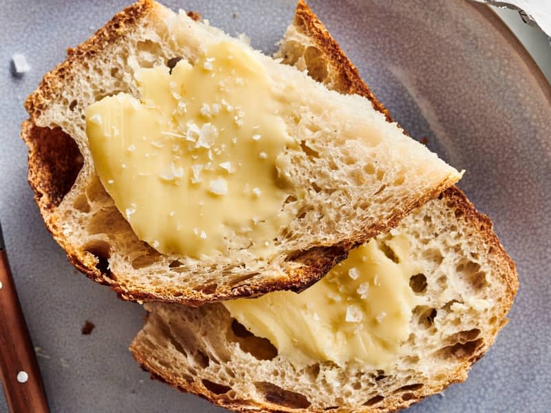 cultured butter is spread on top of toast that sits on a plate with knife and butter package next to it