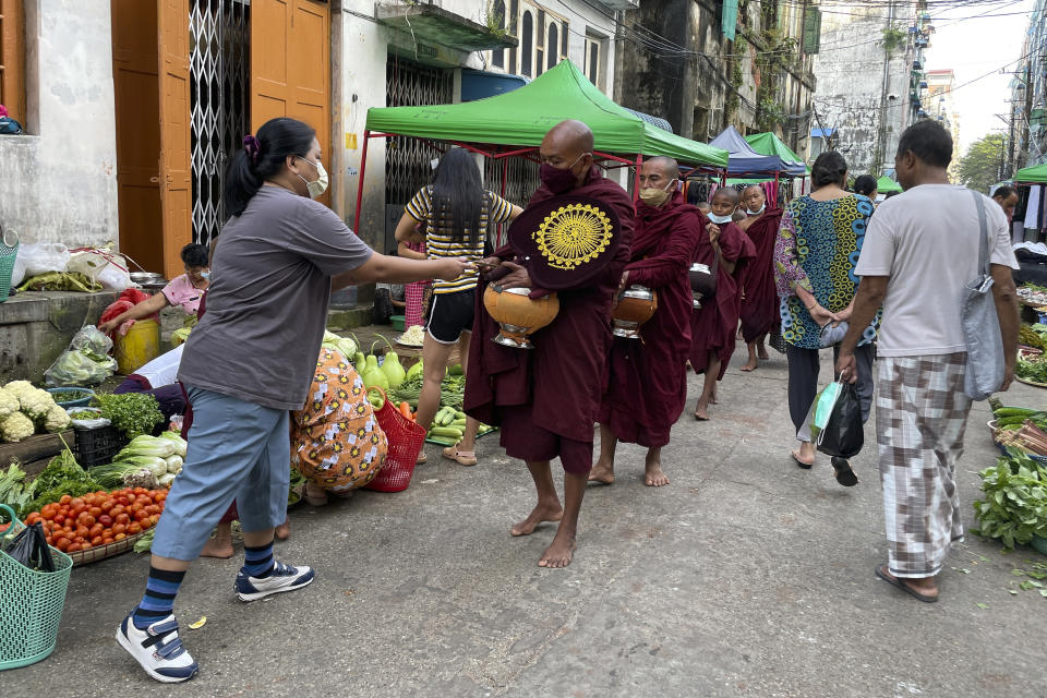 Buddhist monks collect alms from people during their morning walk at the Bogalay Zay Market in Botahtaung township in Yangon, Myanmar on Nov. 12, 2021. The military takeover in Myanmar has set its economy back years, if not decades, as political unrest and violence disrupt banking, trade and livelihoods and millions slide deeper into poverty. (AP Photo)