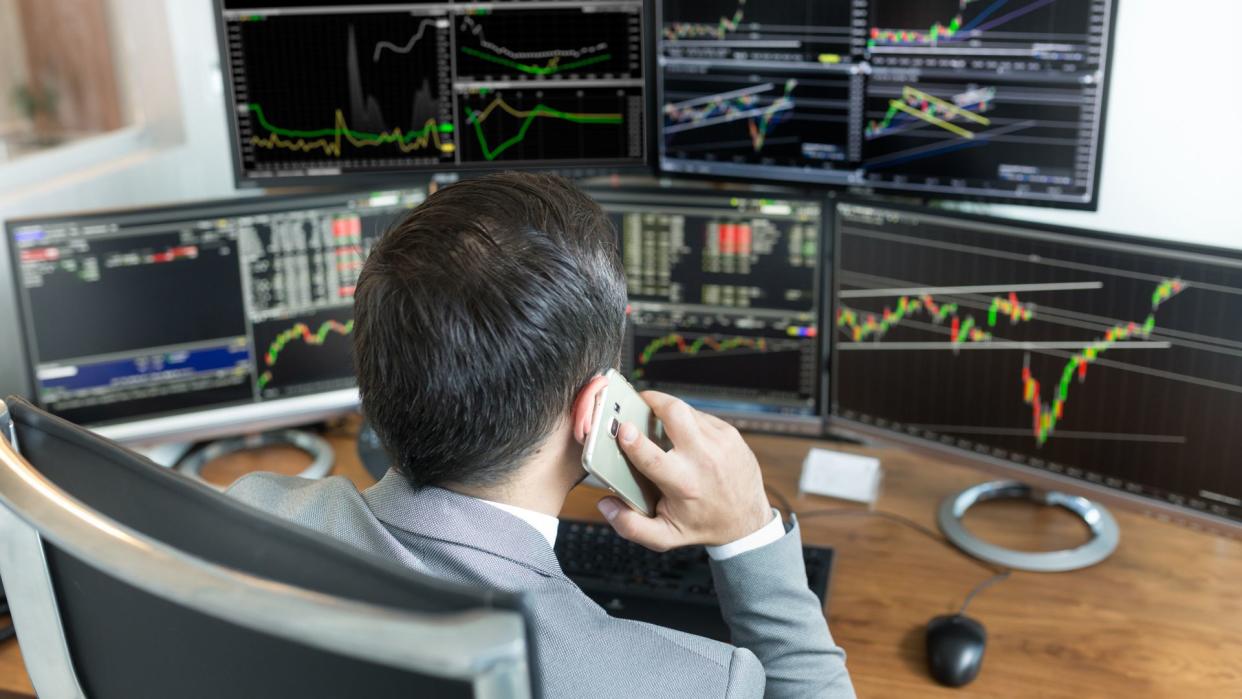 Over the shoulder view of and stock broker trading online while accepting orders by phone.