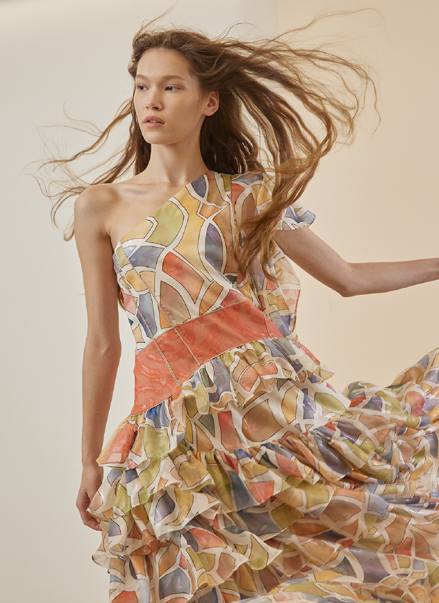 An image from women's wear brand Cahiers' SS 2023 collection features a woman wearing a colorful print on a flowy dress with ruffles.