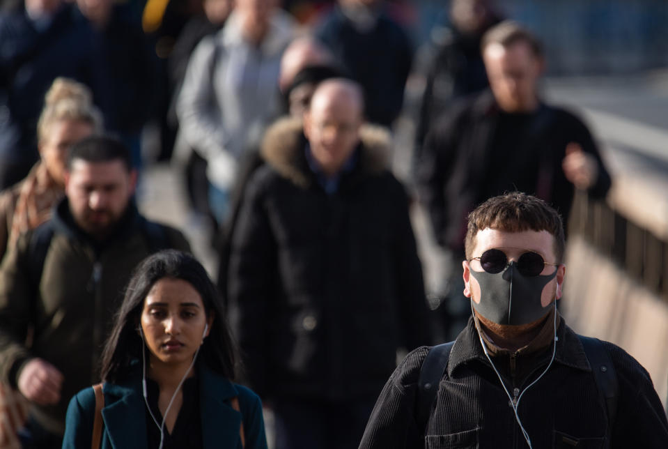 A man wearing a protective face mask as commuters cross London Bridge during morning rush hour in London , as the Government's top scientist warned that up to 10,000 people in the UK are already infected.