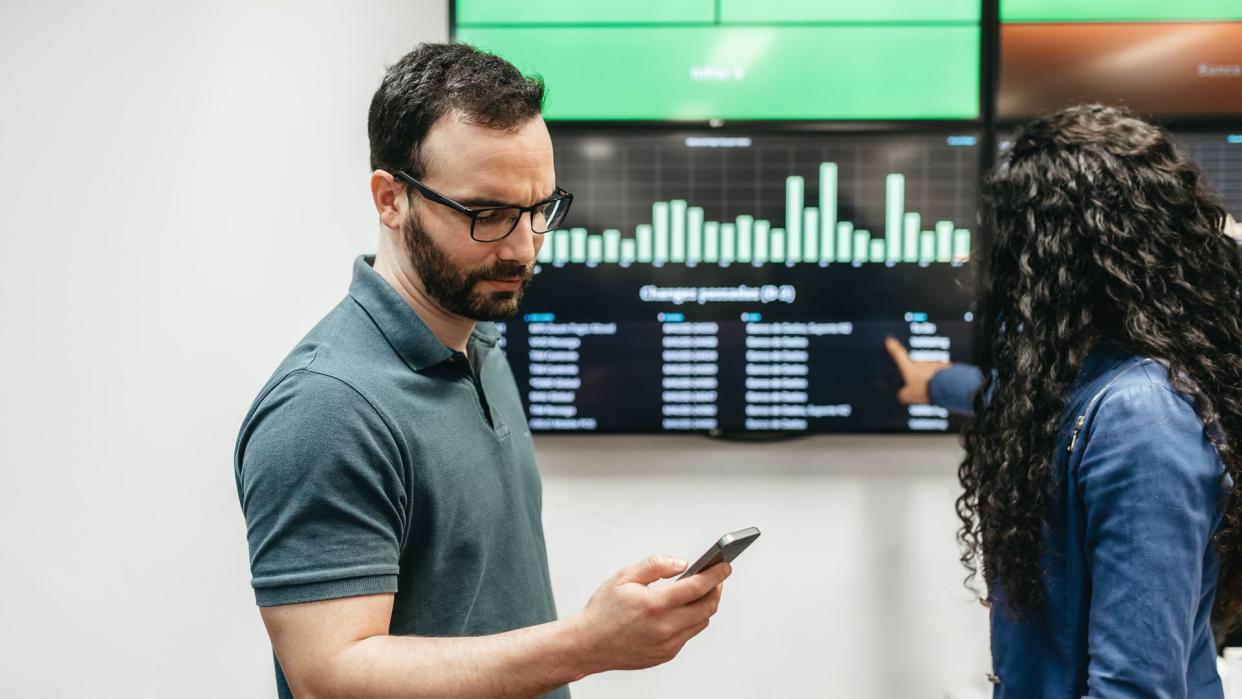 two young business people checking data on mobile and chart screen in office.